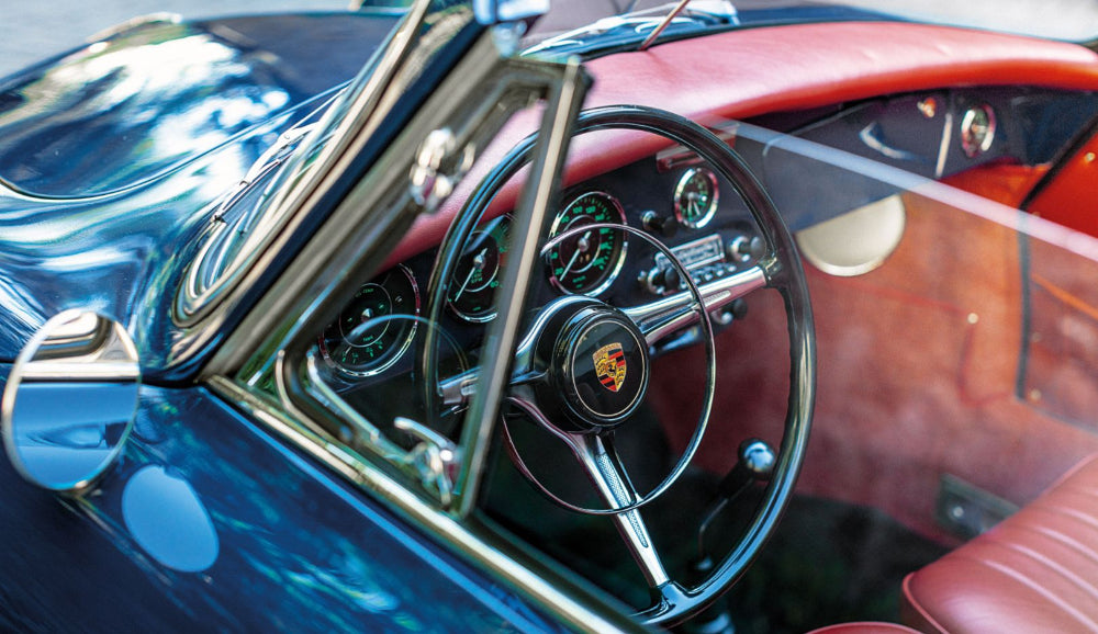 Close-up of a classic car's steering wheel and dashboard with a visible Porsche logo.