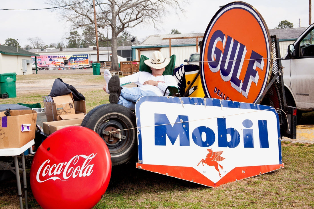 Vintage porcelain enamel signs outside leaned against tires with coca cola enamel button sign and a chevron shield mobil gas porcelain sign and a large gulf orange and blue double sided porcelain metal steel gas station advertising