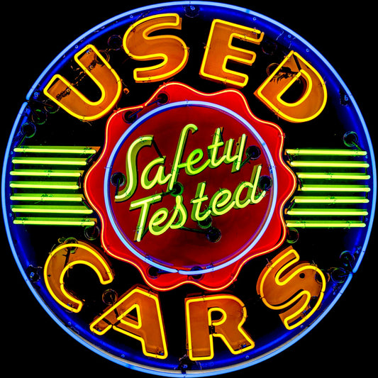 Neon sign advertising 'Used Cars' with 'Safety Tested' in the center.
